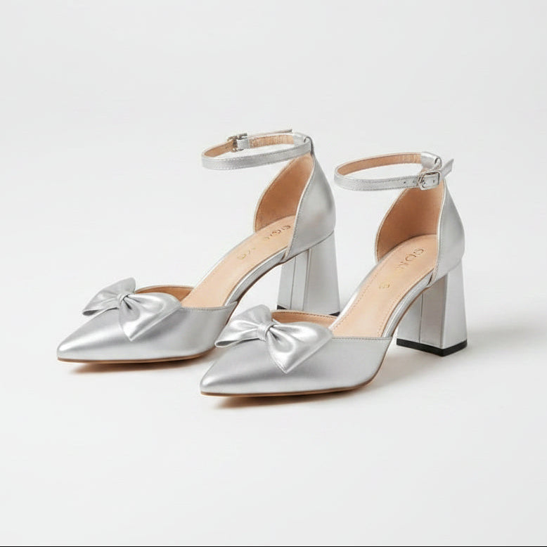 Silver high-heeled shoes with bow details worn by a person in a white lace dress.