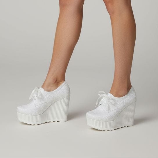 Person wearing a white skirt and white platform shoes on a plain background