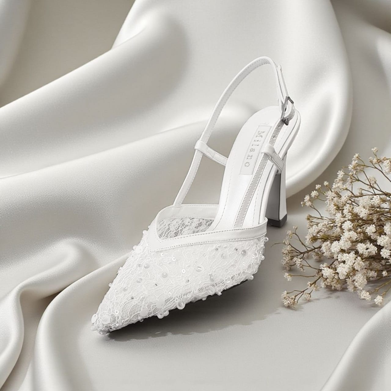 White wedding shoe with lace details on a white fabric background