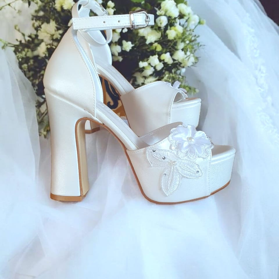 White wedding shoes with floral details on a white fabric background