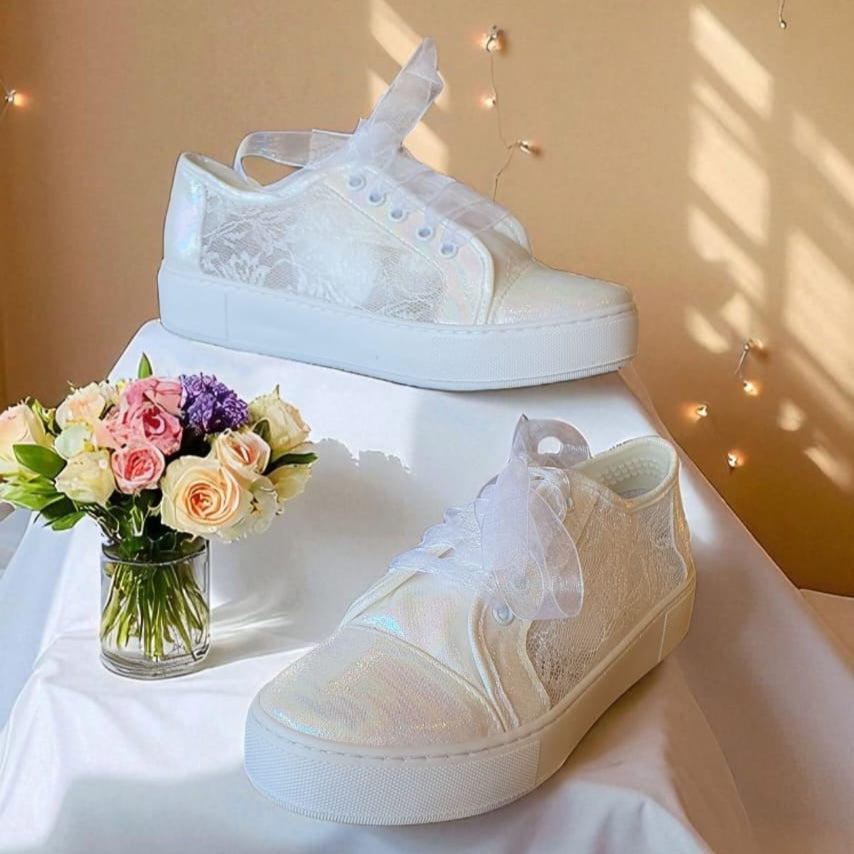 White Lace sneakers on a white surface with a vase of flowers in the background