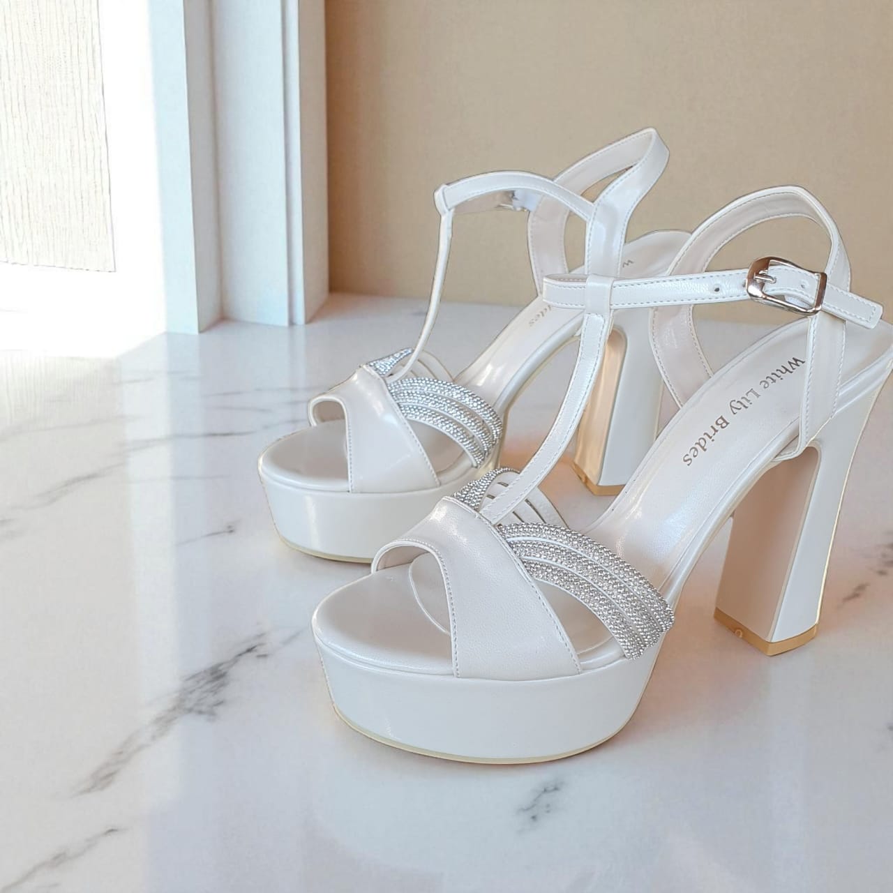 Pearl White high-heeled shoes with glittery straps on a marble surface