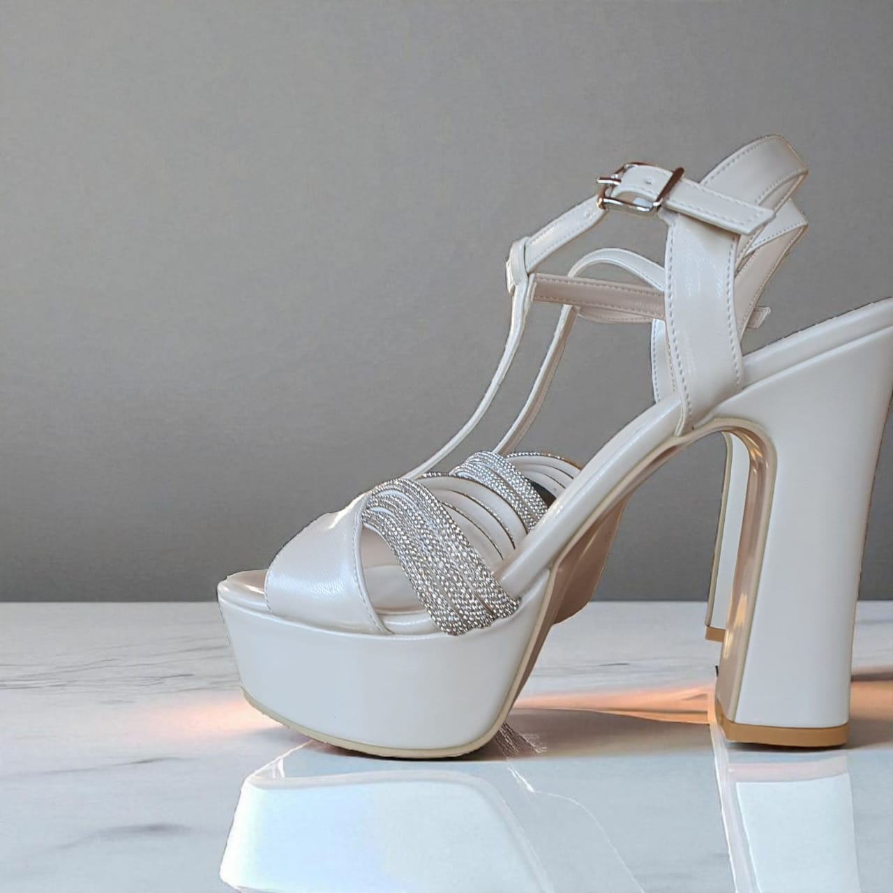 White high-heeled sandal with platform and rhinestone details on a reflective surface.