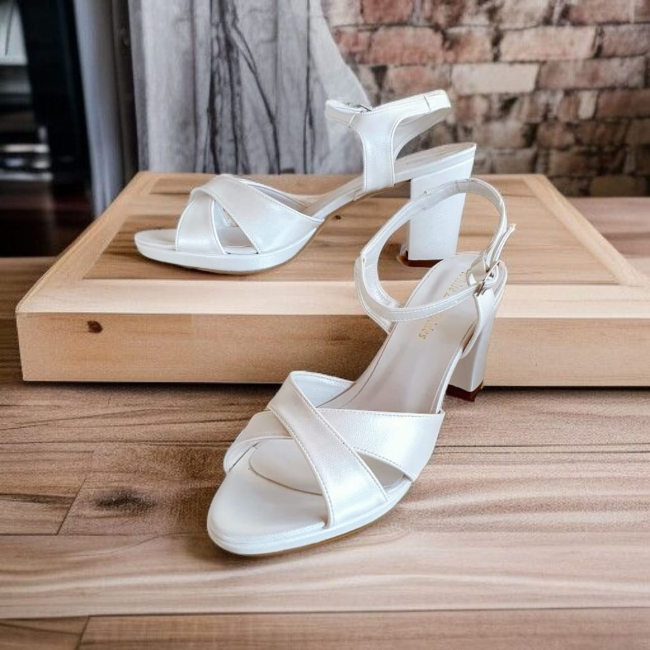 White strappy sandals on a wooden surface with a brick wall background