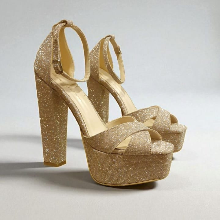 Gold glitter high-heeled shoes on a light gray background