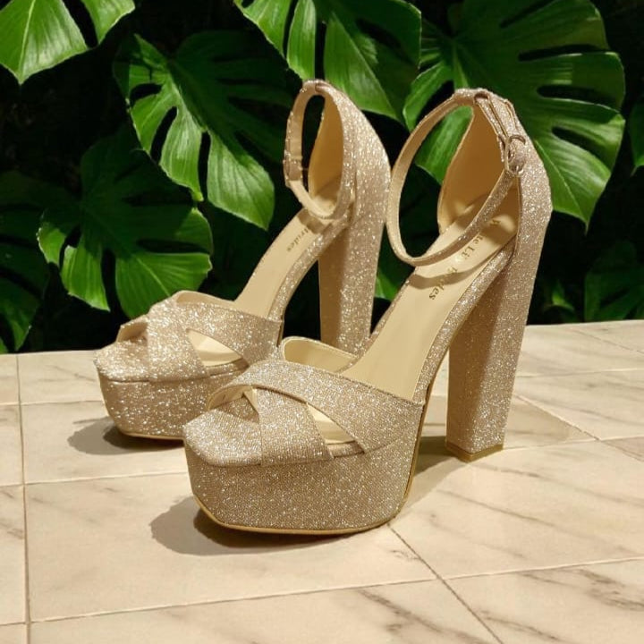 Gold glitter high-heeled shoes on a marble surface with green leafy background