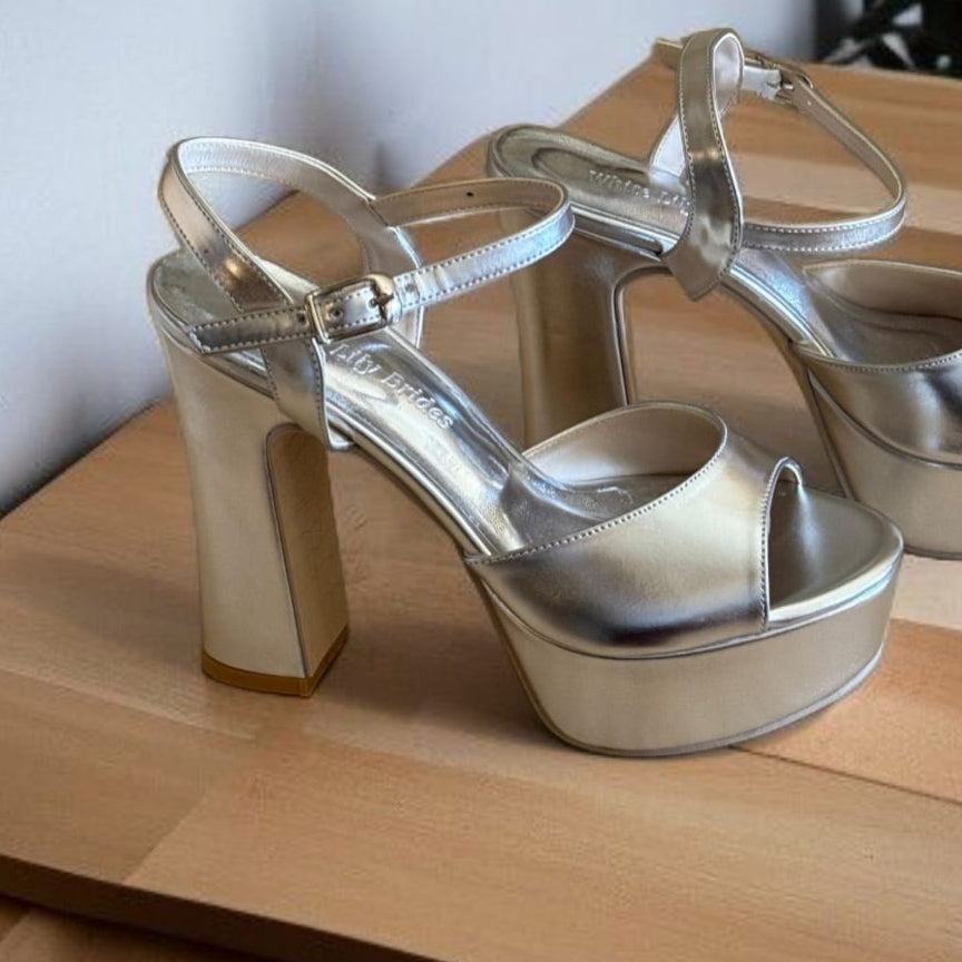 Silver high-heeled shoes on a wooden surface with a plant in the background