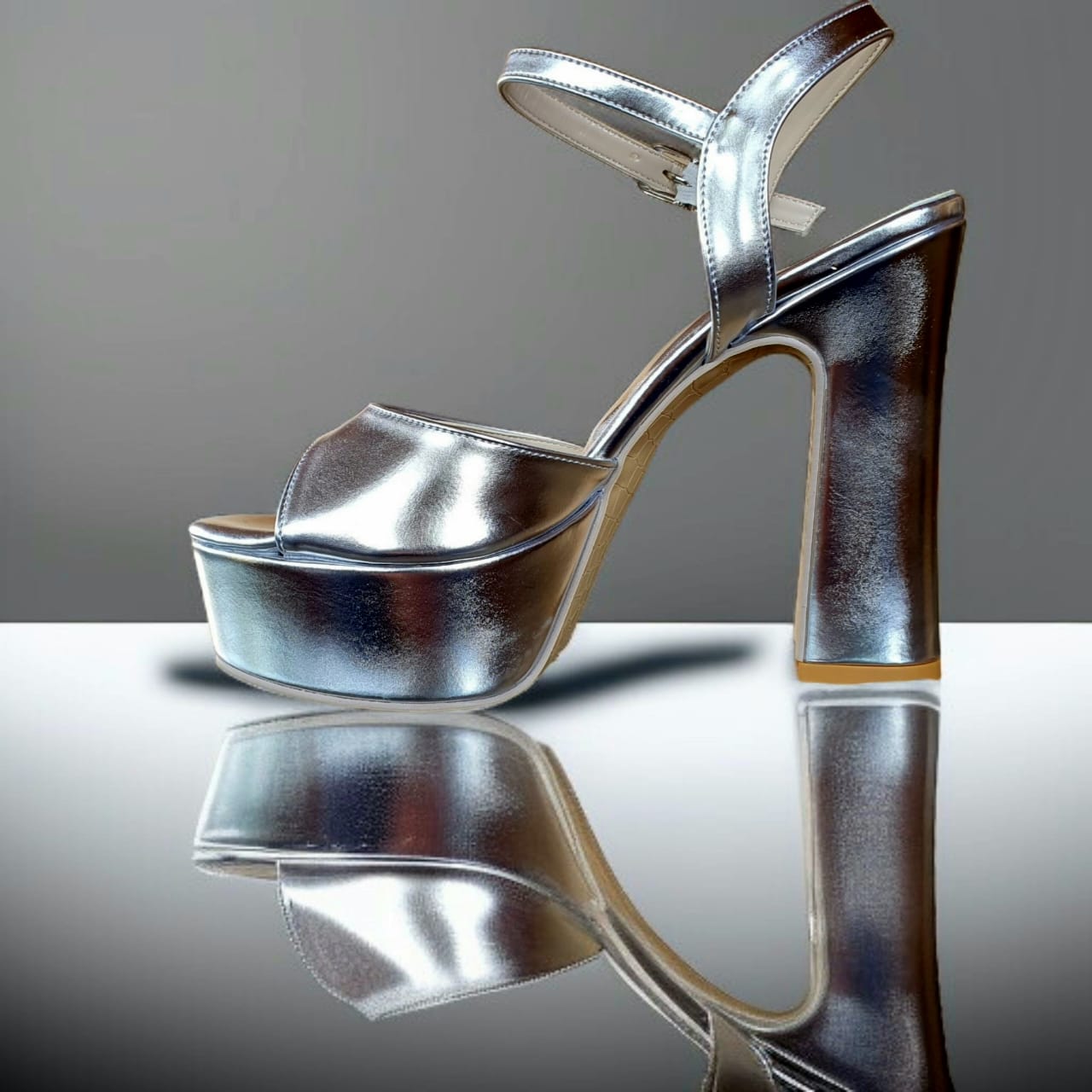 Silver high-heeled shoe on a reflective surface with a gray background