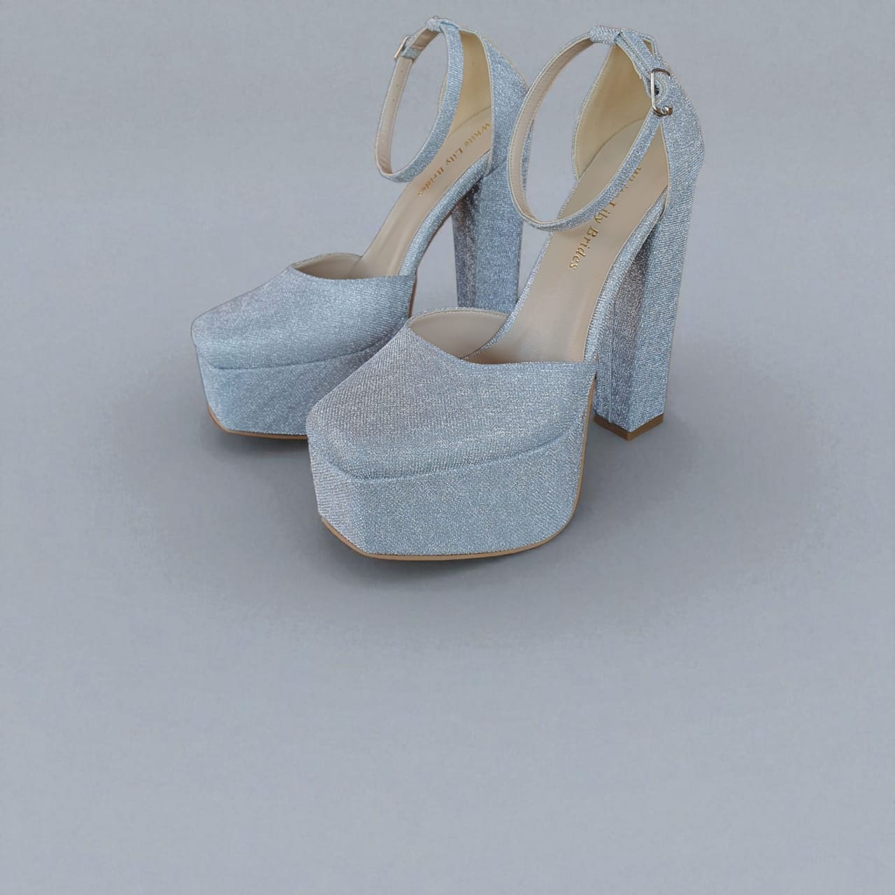 Pair of silver glittery high-heeled shoes on a gray background