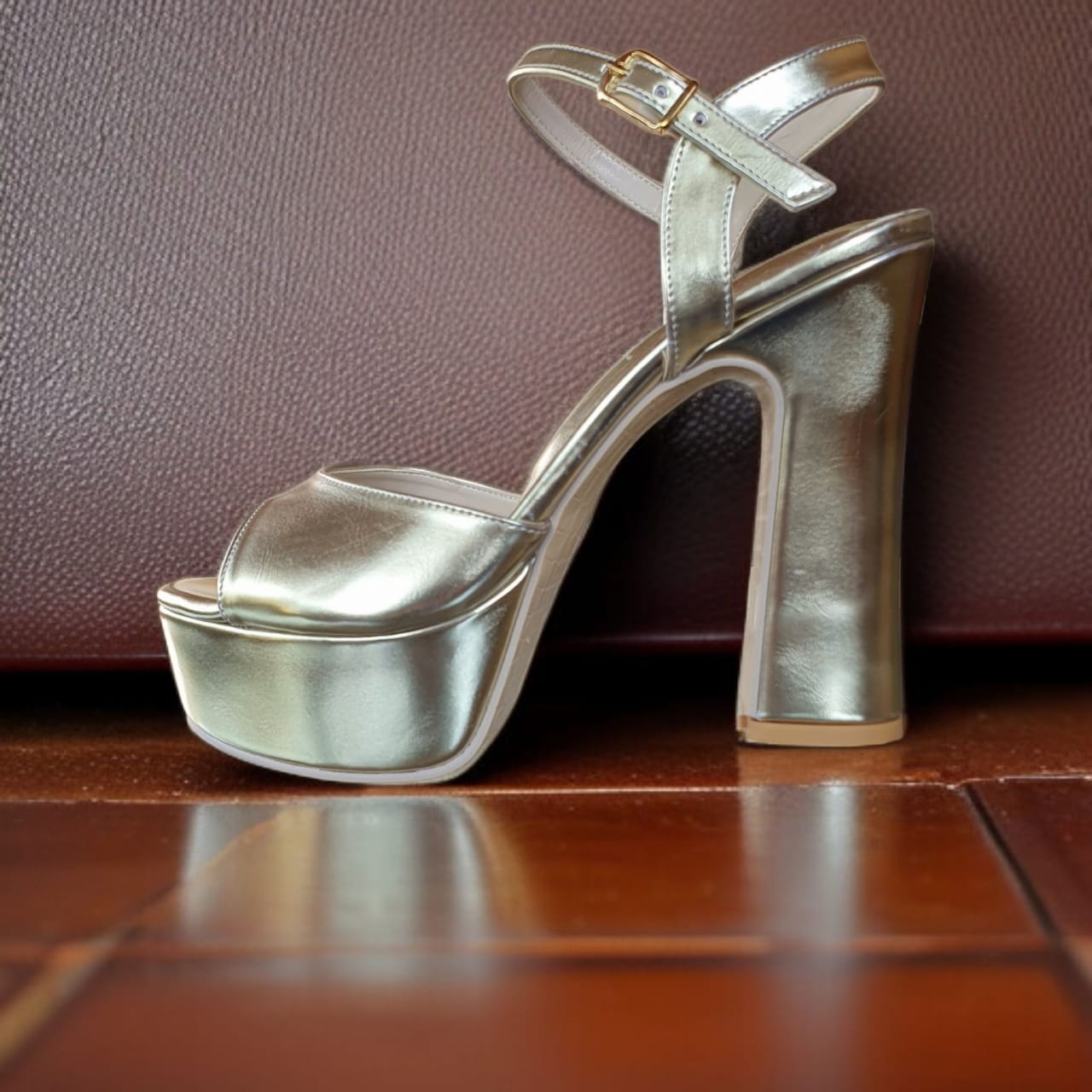 Gold high-heeled platform shoe on a wooden surface with a brown leather background