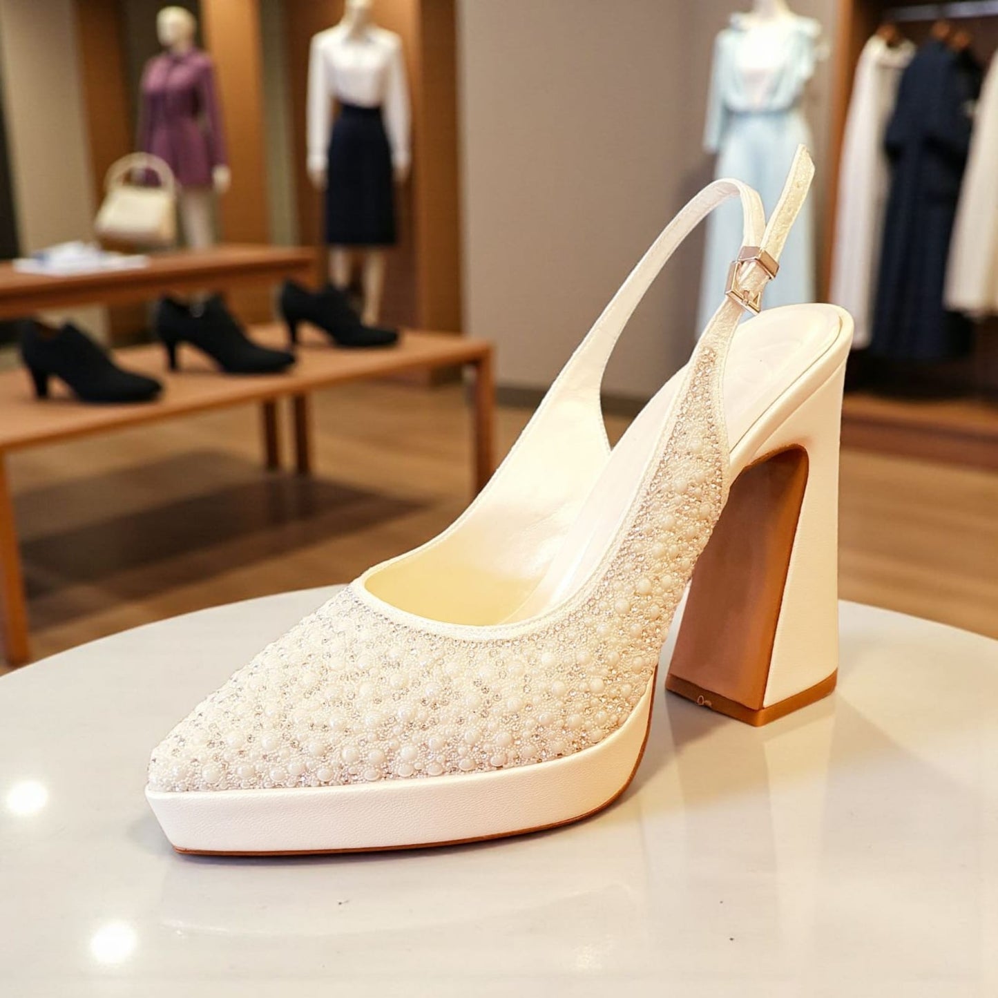 Sparkly high-heeled shoe on a table with mannequins in the background