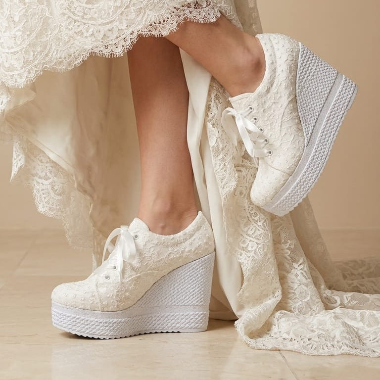 12 cm White lace-up wedge sneakers with textured white platform soles, shown on a model wearing a cream lace dress against a beige background.