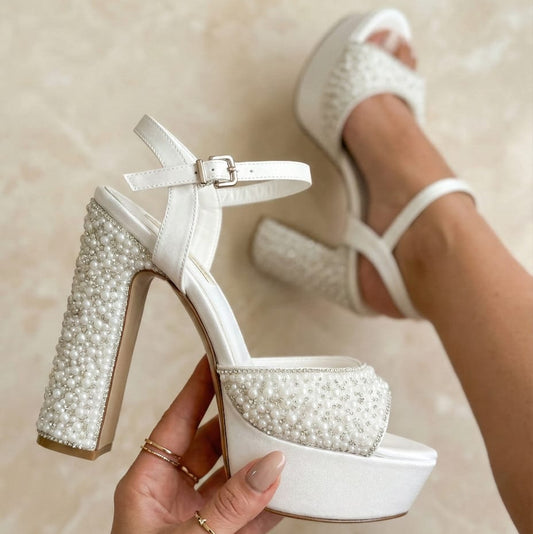 Pearl White high-heeled shoes with pearl embellishments held by a hand against a neutral background Beirut Lobby