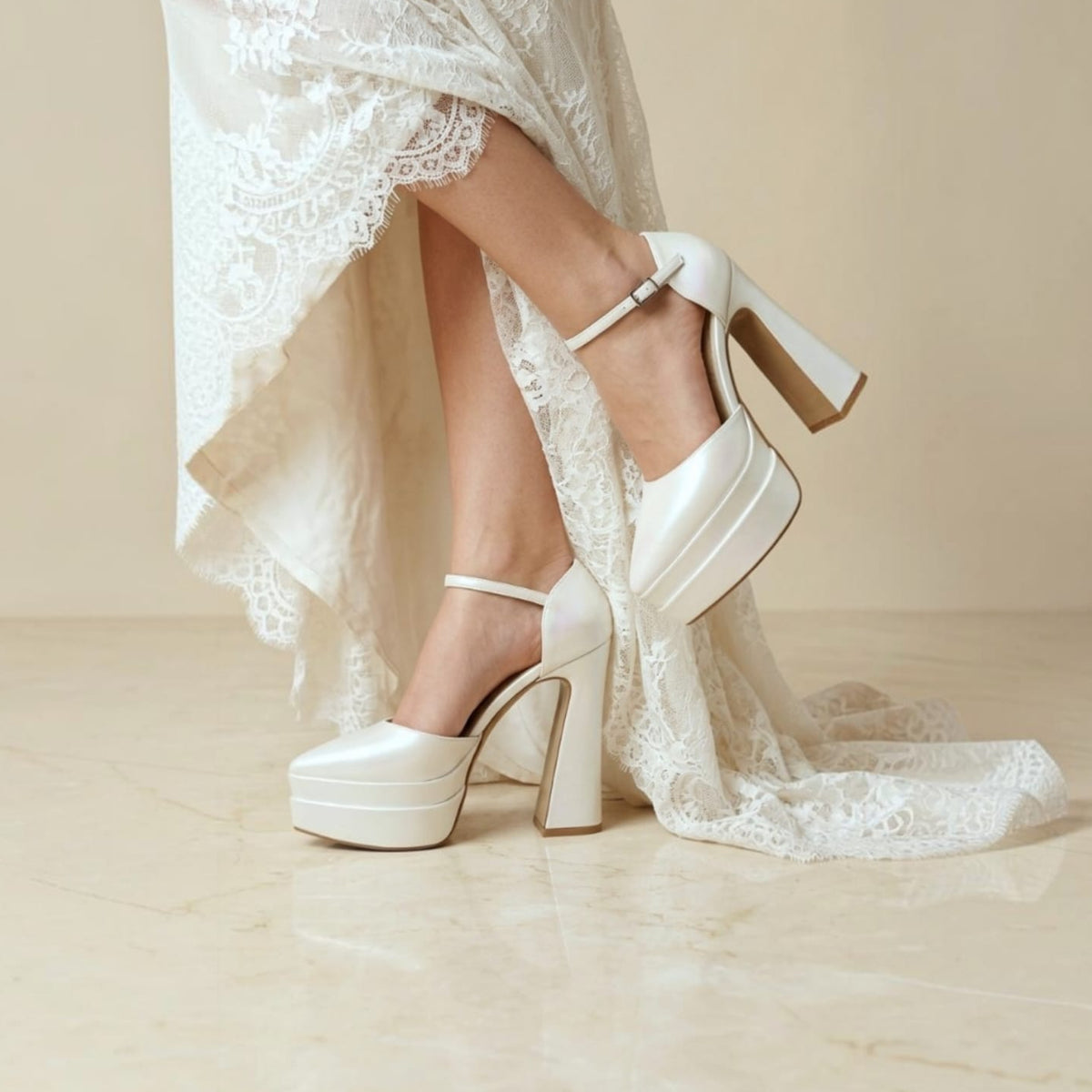 Pearl White platform high-heel mule shoes with ankle straps, shown on a model wearing a white lace bridal gown against a warm beige studio background.