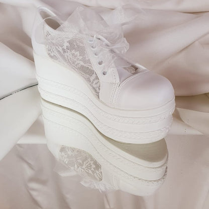White wedding shoes with lace details on a reflective surface