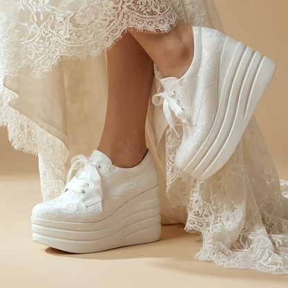 White lace-up platform sneakers worn with a white lace dress, shown on a model against a warm beige background.