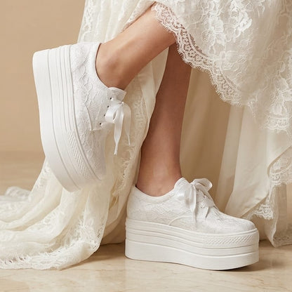 A person wearing white platform lace-up sneakers with white lace-up dress and cream-colored lace-up dress, standing on a beige marble floor.