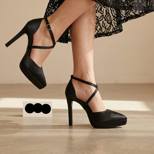 Black platform high-heel pumps with ankle straps worn by a model in a black lace dress, shown against a warm beige studio background with a small label reading 'white Lily Brides'.