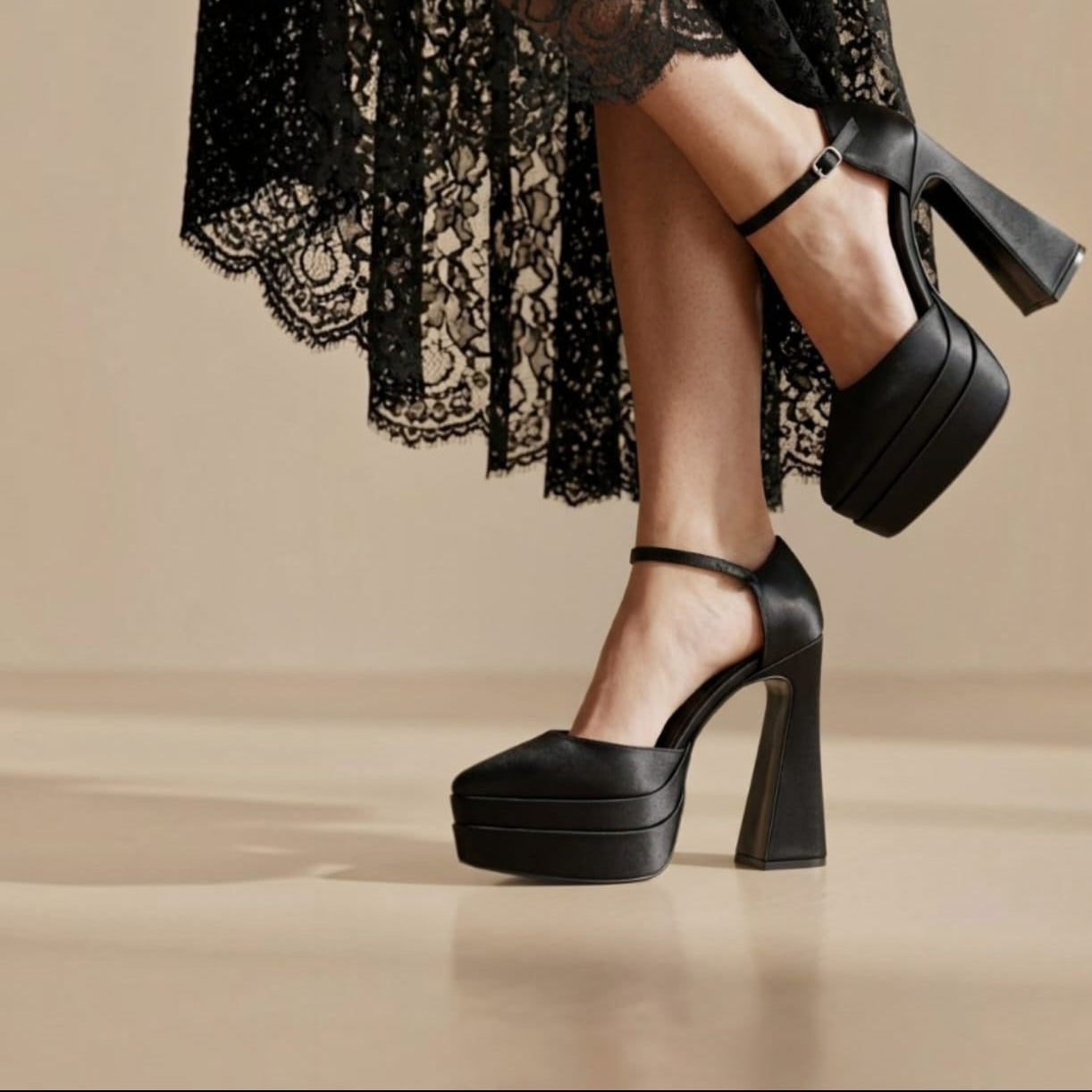 Black platform high-heeled shoes with ankle straps, shown on a model wearing a black lace dress against a warm beige studio background. Beirut