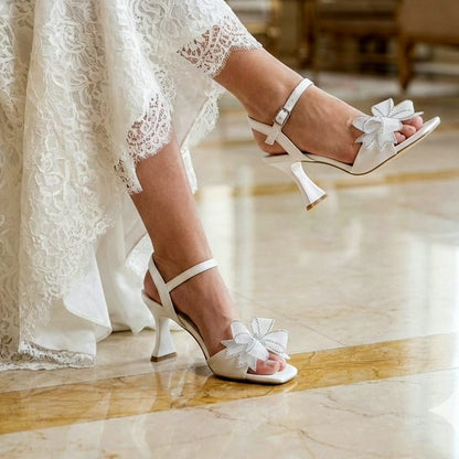 Bridal shoes with decorative bows worn by a person in a lace dress in an elegant room.