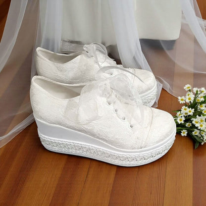 White lace-up shoes on a wooden floor with a white curtain and flowers in the background