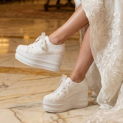 Side view of luxury white lace platform wedding sneakers with ribbon laces, worn by a bride sitting in a luxury lobby in Beirut, Lebanon, highlighting the detailed floral texture and high wedge sole.