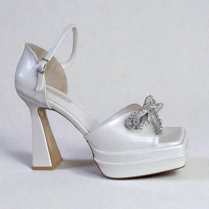White matte platform bridal heels with crystal-embellished bow and thick block heel.