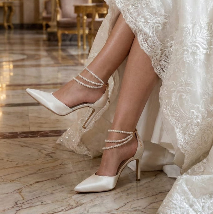 10cm Pearl White high-heeled bridal shoes with ankle straps worn by a bride in an elegant indoor setting.