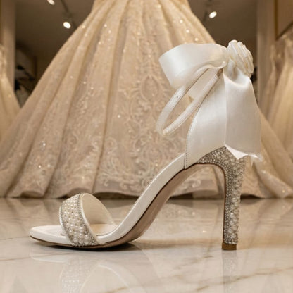 Pearl White high-heeled shoe with a bow in front of a wedding dress