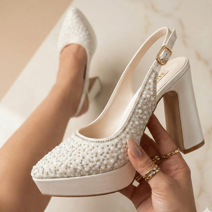 Pearl White high-heeled shoes with pearl embellishments held by a hand against a neutral background in Beirut