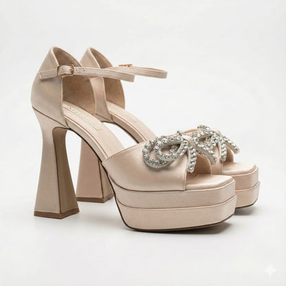 Side view of a champagne shimmer platform high heel shoe with a crystal bow embellishment and ankle strap