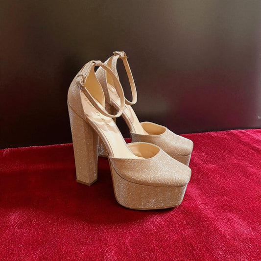 Gold glittery high-heeled shoes on a red surface with a dark background