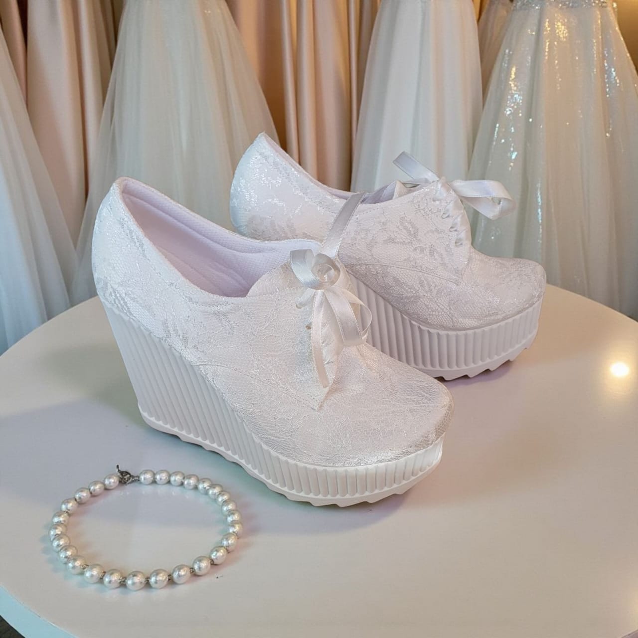 White lace platform shoes with bows and a pearl bracelet on a light surface.