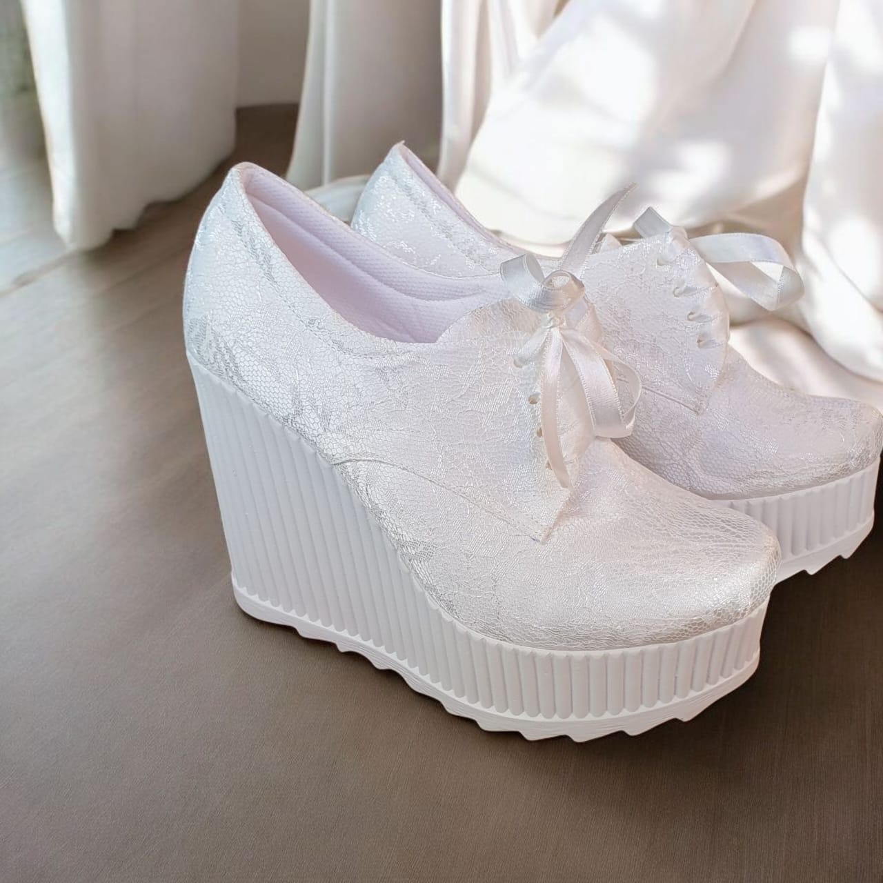 White lace-up wedge shoes with ribbed sole on a light wooden floor.