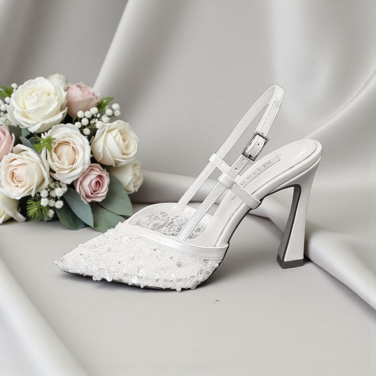 White wedding shoe with lace details next to a bouquet of flowers on a gray background