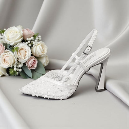 White wedding shoe with lace details next to a bouquet of flowers on a gray background