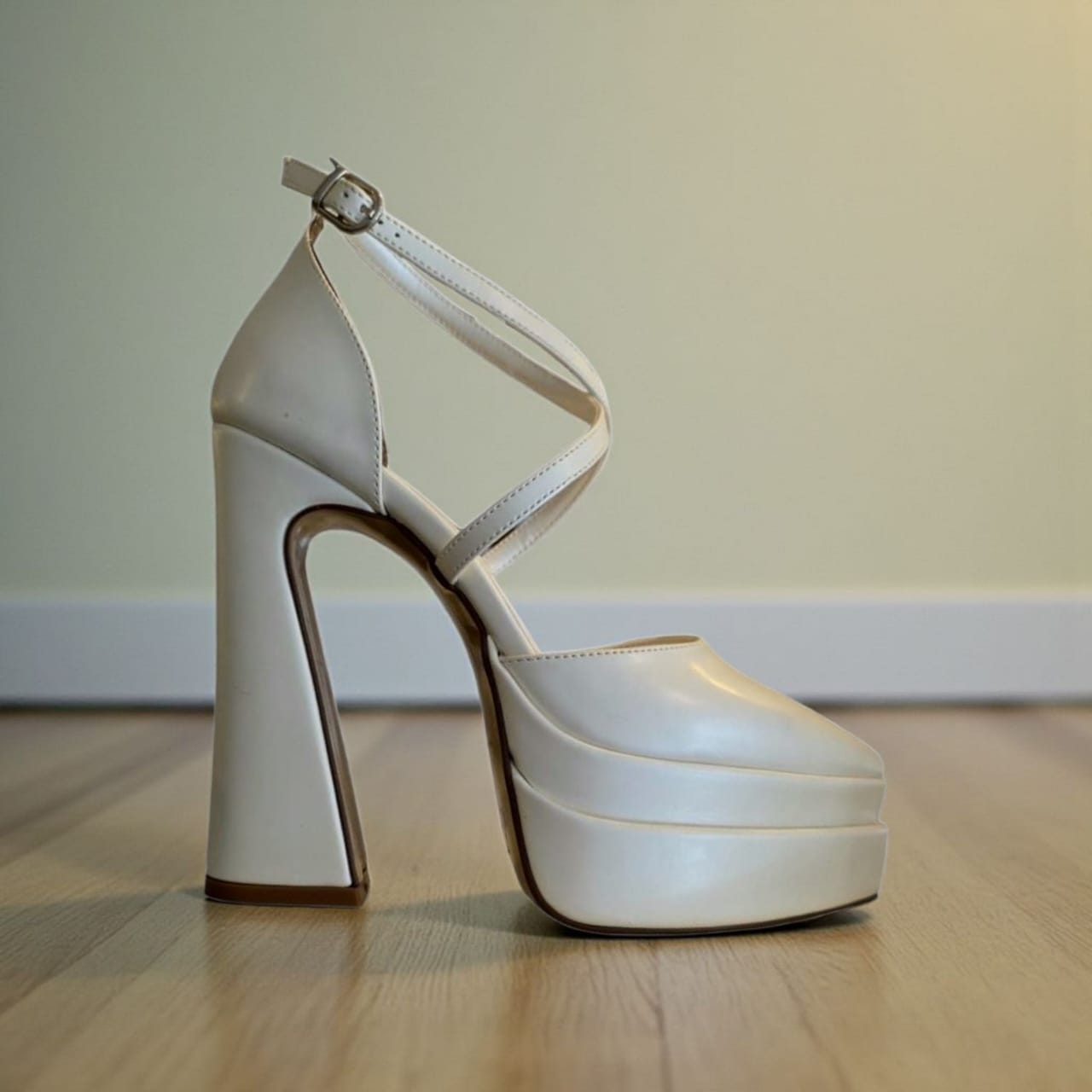White high-heeled platform shoe on a wooden floor with a neutral background