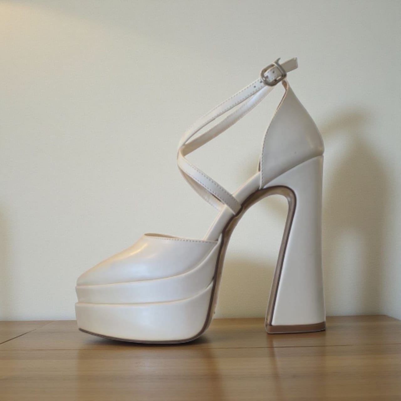 White high-heeled platform shoe on a wooden floor with a plain background
