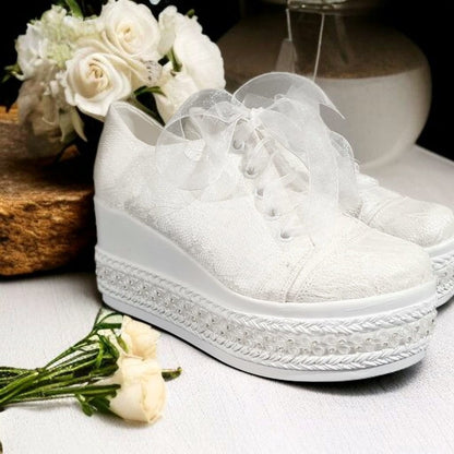 White platform sneakers with decorative laces on a surface with white flowers.