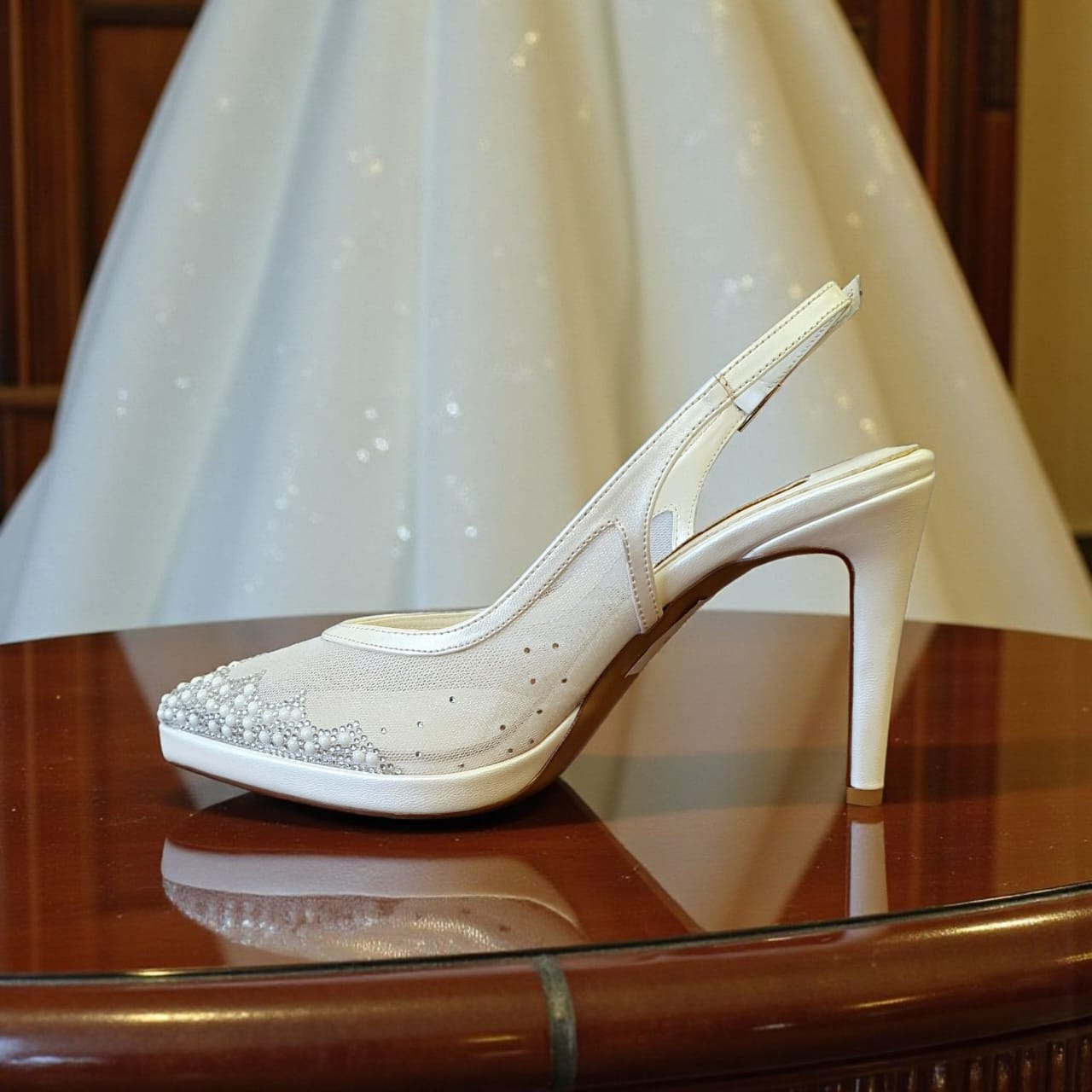 White high-heeled shoe with decorative elements on a reflective surface