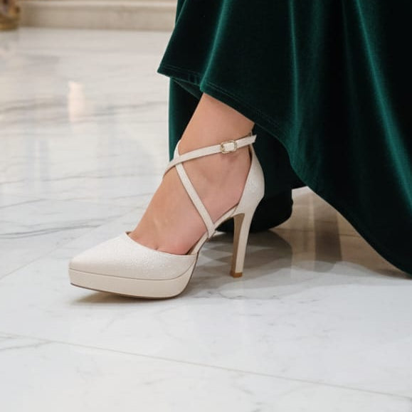 Person wearing a green dress and white high-heeled shoes in an elegant interior setting.