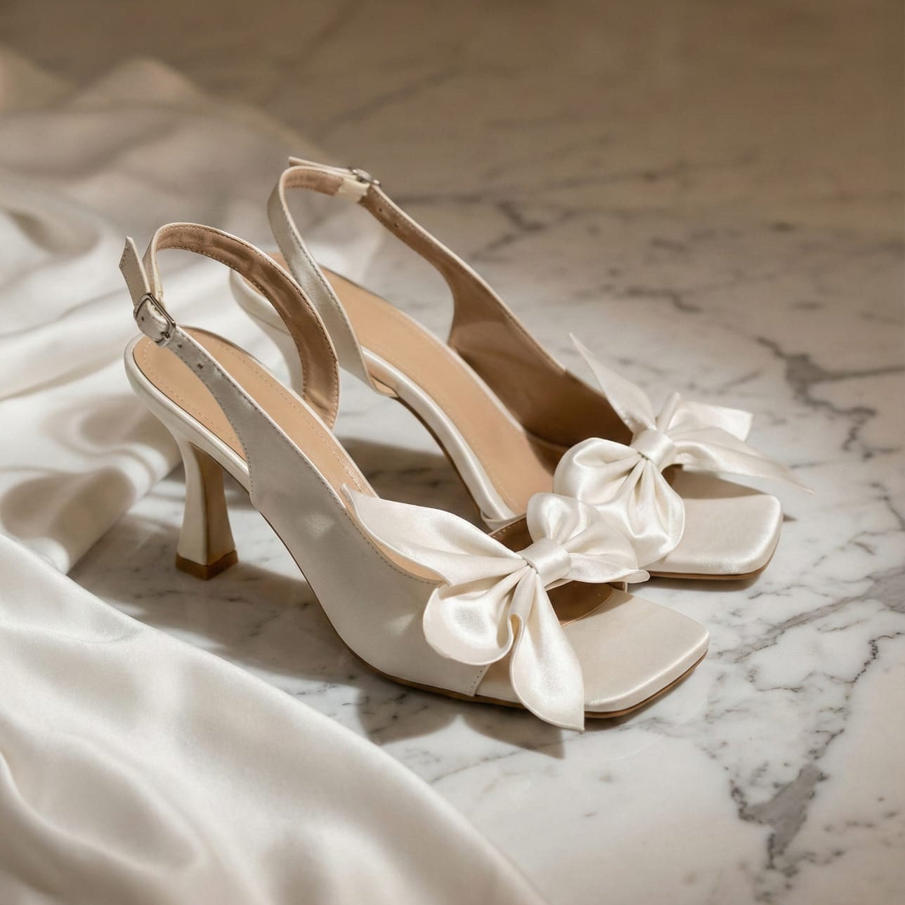 White high-heeled shoes with satin bows on a marble surface