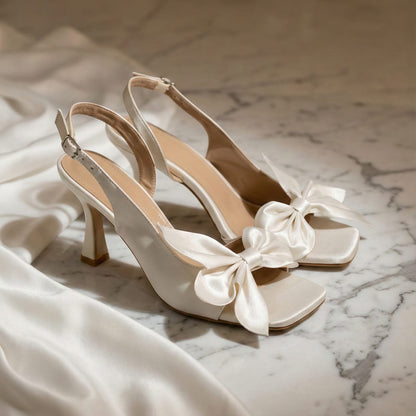 White high-heeled shoes with satin bows on a marble surface