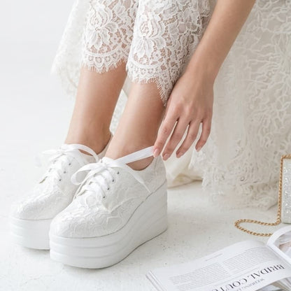 White lace-up sneakers worn with a white lace dress on a light surface.