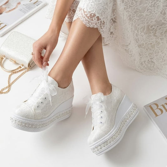 White sneakers with embellishments worn by a person in a white lace dress on a light background.