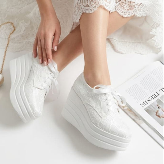 White sneakers worn with a white lace dress on a light background