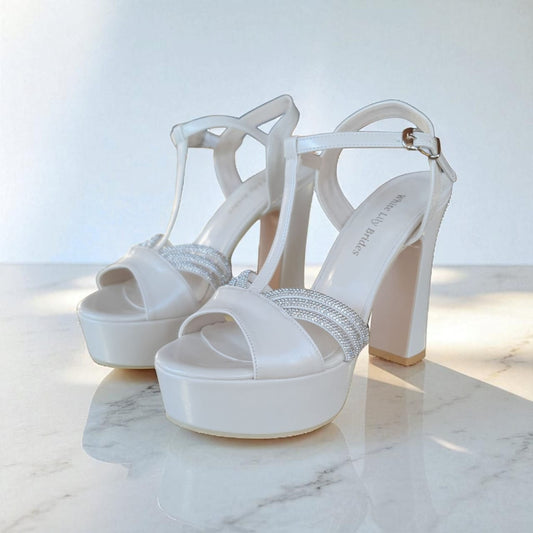 White high-heeled sandals with decorative straps on a marble surface