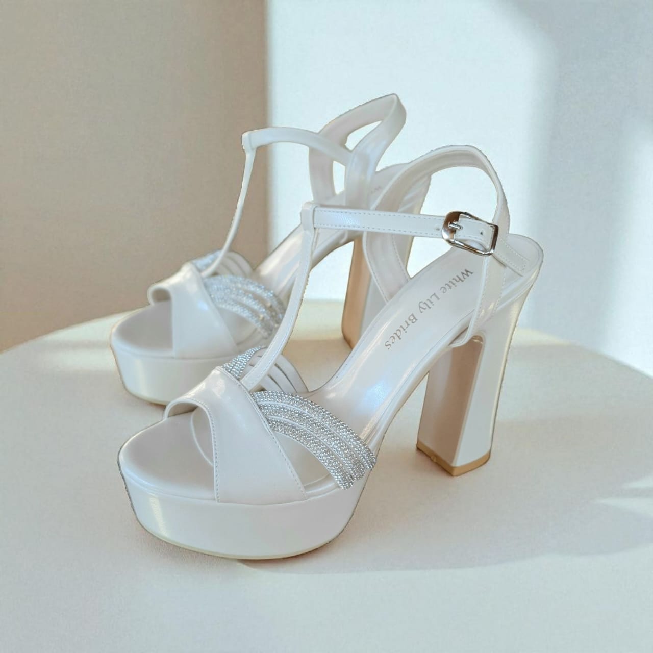 Pearl white high-heeled shoes with platform and thin straps on a light background