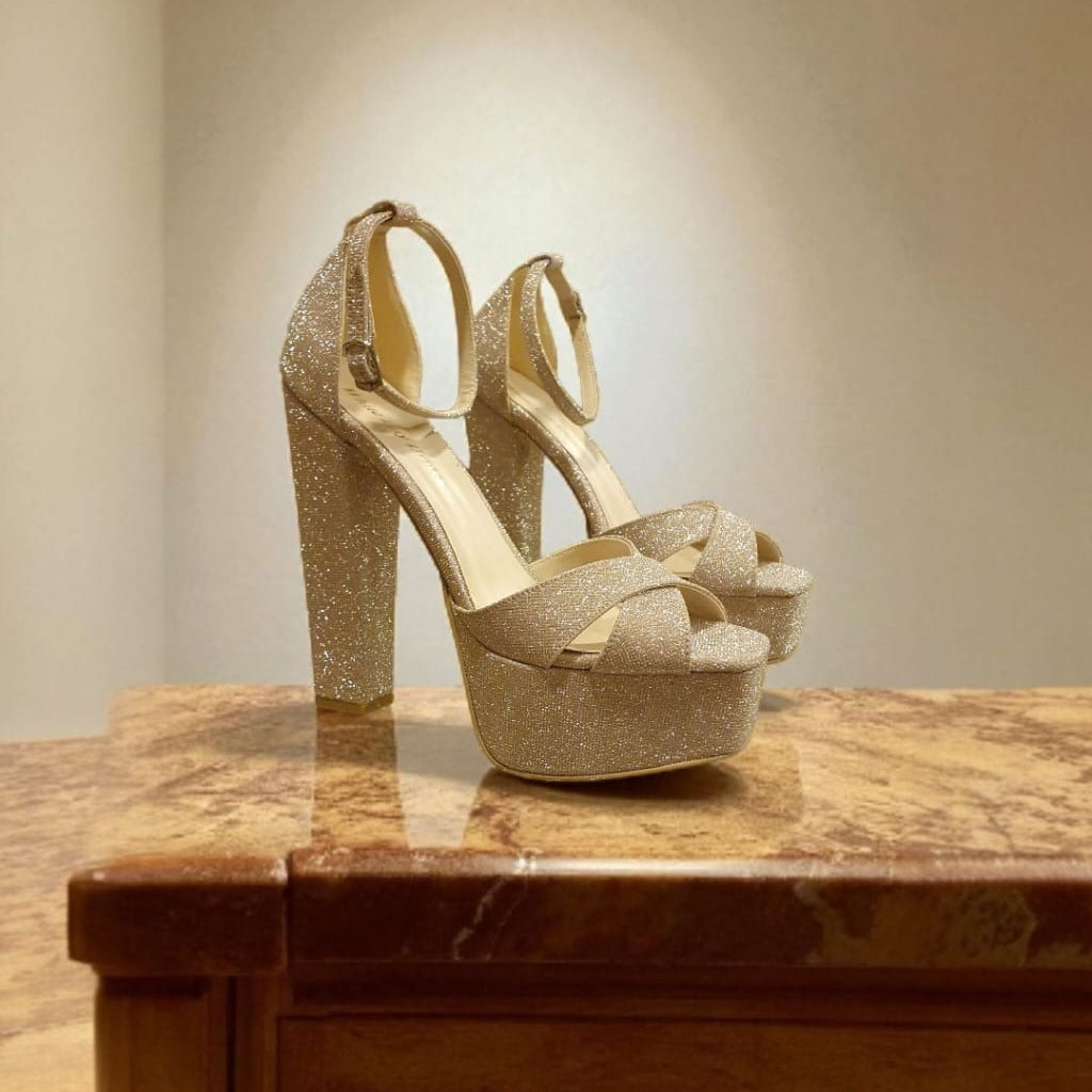 Gold glitter high-heeled shoes on a marble surface with a neutral background