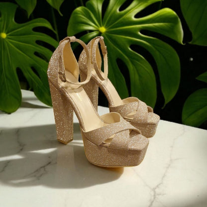 Gold glitter high-heeled shoes with bow detail on a marble surface with green leaves in the background